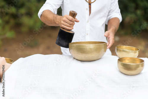 Male hands with Nepal Buddha singing bowl, close up. A man wearing in white, master of healing sound massage, doing sound therapy with tibetan singing bowl, alternative medicine, mental health