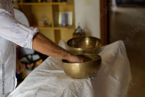 Tibetan singing bowls master doing sound healing massage with Nepal Buddha singing bowl at home. A man in white practice sound therapy, selective focus