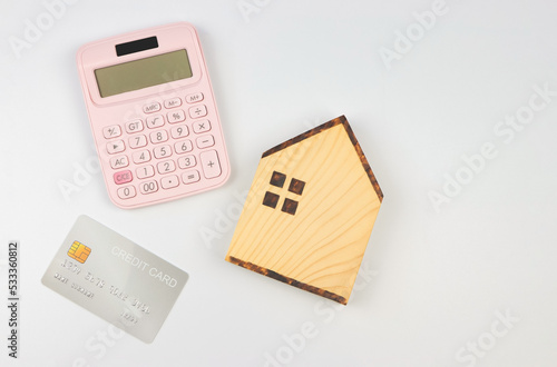 flat layout of wooden house model , pink calculator and credit card on white background with copy space. home purchase concept.