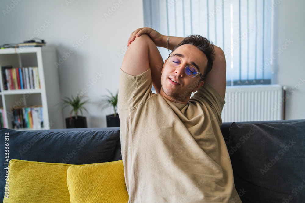 A young man having head back and neck pain in his home office while sitting on the couch during the day A young man having head back and neck pain in his home office while sitting on the couch during the day
