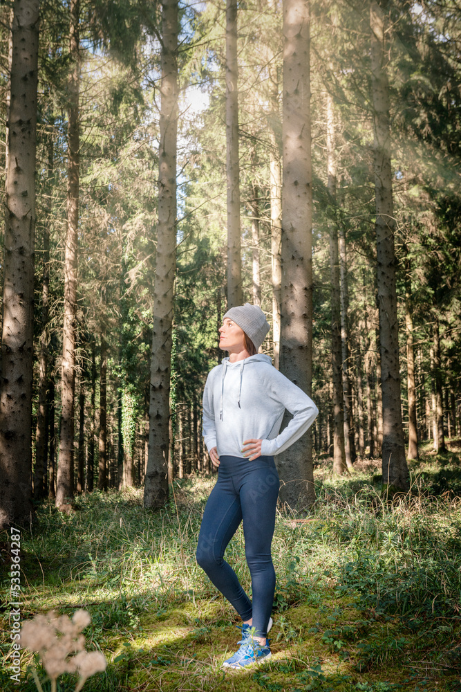 Sporty woman standing with her hands on her hips, resting after running in woodland. Sporty woman standing with her hands on her hips, resting after running in woodland.
