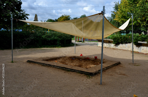 there is a tarpaulin between two wooden pillars. roof serving as a shading for the sandpit or terrace at the house or restaurant in the front garden and in the park. metal wires and cords
