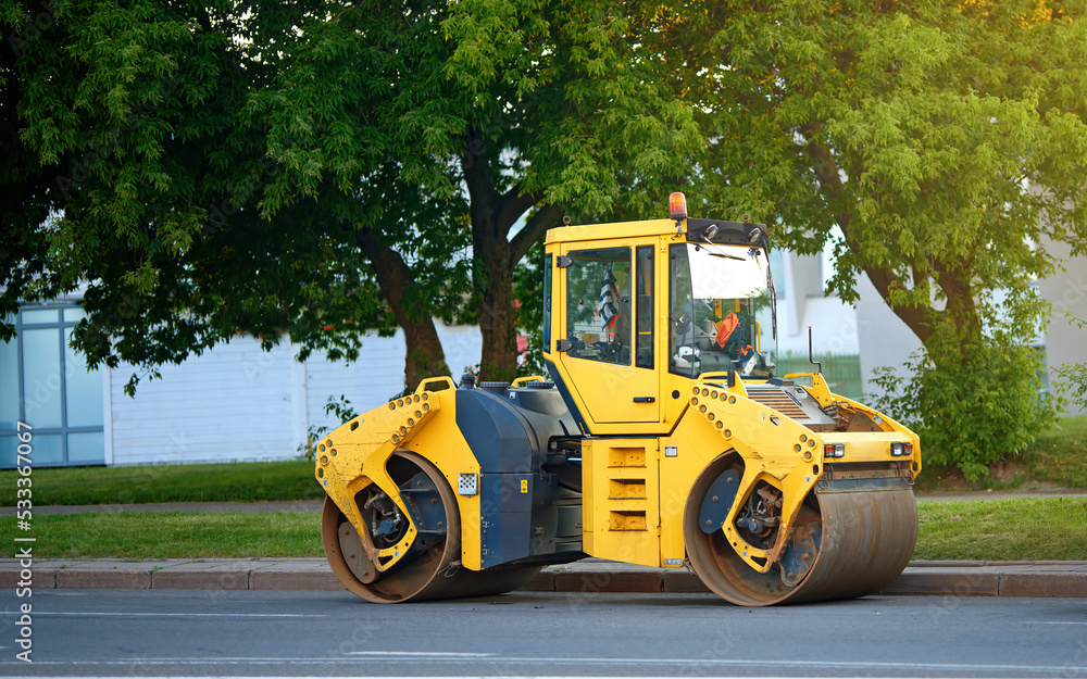 Asphalt roller side view. Road repair work, paving asphalt. Asphalt compactor parked at roadway. Road engineering, yellow road roller asphalt repair work.