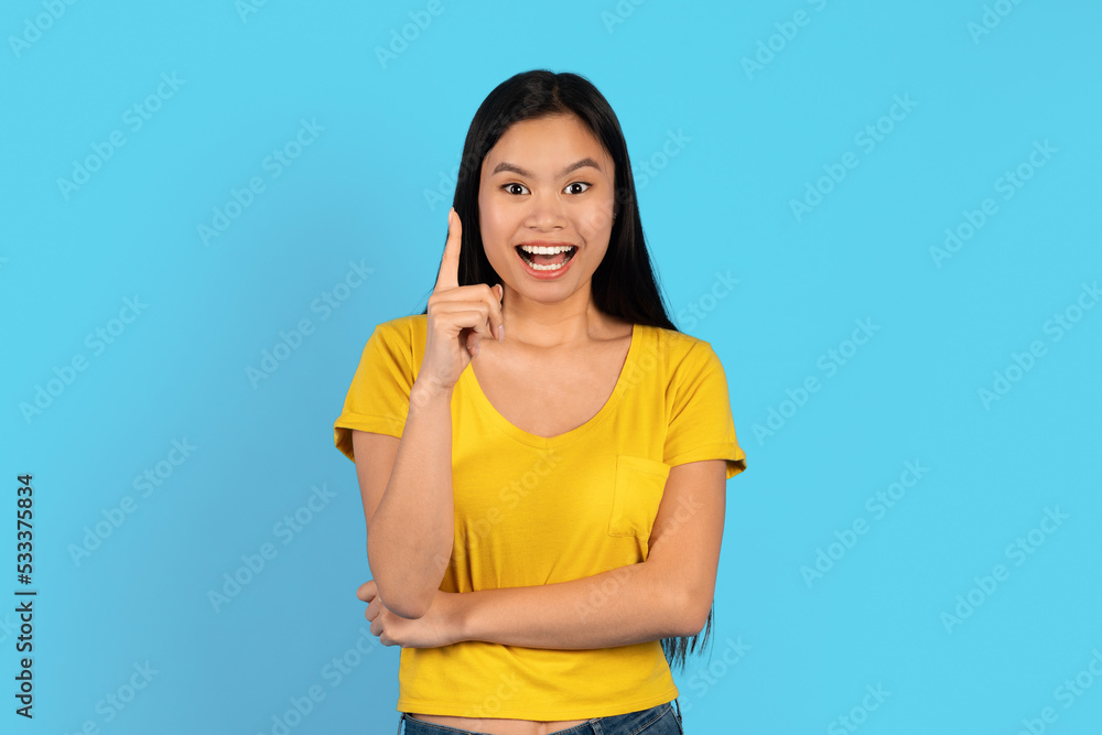 Glad inspired young japanese lady in yellow t-shirt with open mouth, show finger up on empty space, got idea Glad inspired young japanese lady in yellow t-shirt with open mouth, show finger up on empty space, got idea