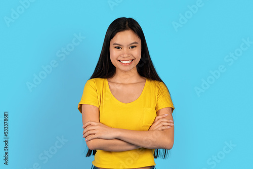 Cheerful confident pretty young chinese female in yellow t-shirt with crossed arms on chest look at camera