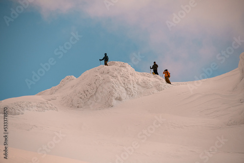 incredible snow-covered mountain slope with ledge with skiers on it.