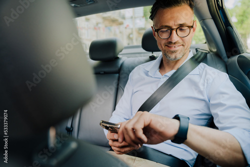European grey man looking at smartwtch and using mobile phone at car