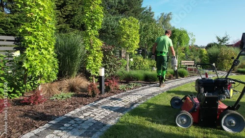 Caucasian Gardener Blowing Dirt and Leafs From Garden Cobble Paths photo