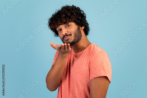 Handsome young indian guy sending fly kiss, blue background