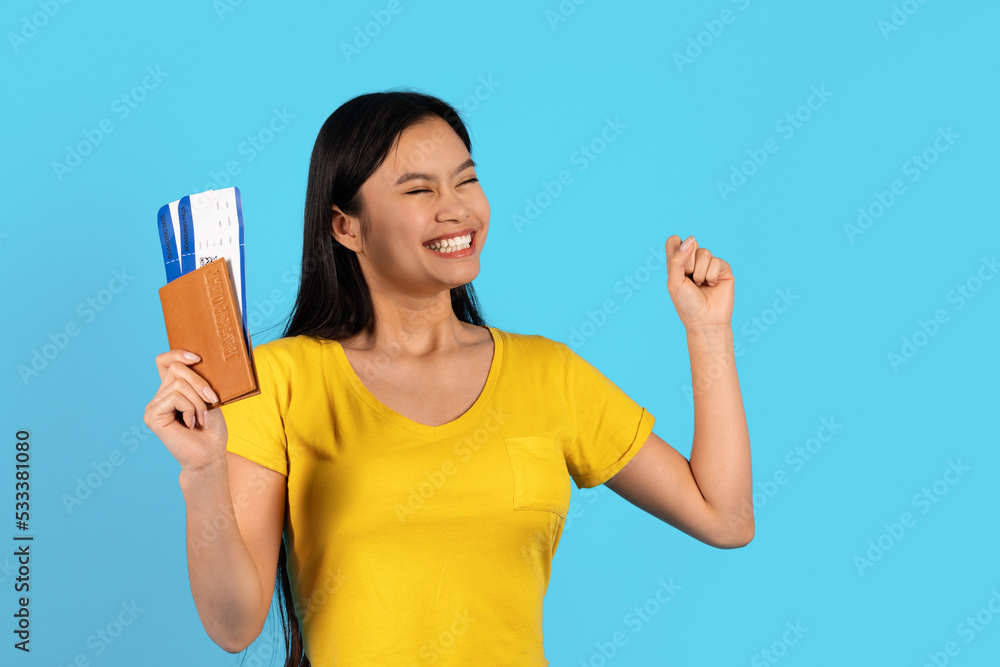 Satisfied excited young chinese female in yellow t-shirt with passport, air tickets looks at empty space Satisfied excited young chinese female in yellow t-shirt with passport, air tickets looks at empty space