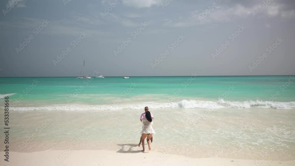 Latin american couple enjoys a vacation and spinning around on the tropical beach. Turquoise water and white sand. Slow motion shot Latin american couple enjoys a vacation and spinning around on the tropical beach. Turquoise water and white sand. Slow motion shot