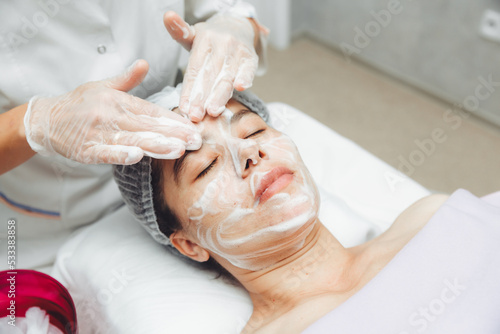 the cosmetologist cleanses the skin with foam. A woman s skin care procedure. Natural cosmetics. A beautiful face. Cosmetic treatment of the face. Therapeutic peeling cream.