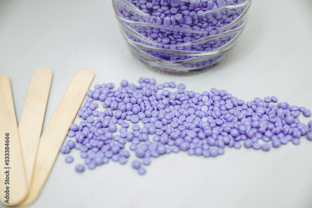 Close-up of lilac and pink wax granules scattered from a jar. Cosmetic procedure to remove unwanted hair from the body. depilation and epilation. Close-up of lilac and pink wax granules scattered from a jar. Cosmetic procedure to remove unwanted hair from the body. depilation and epilation.