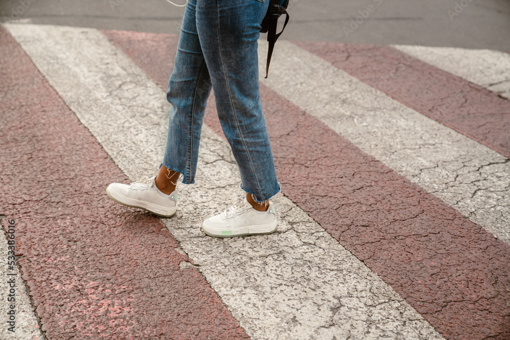 Young black woman wearing jeans walking on pedestrian crossing