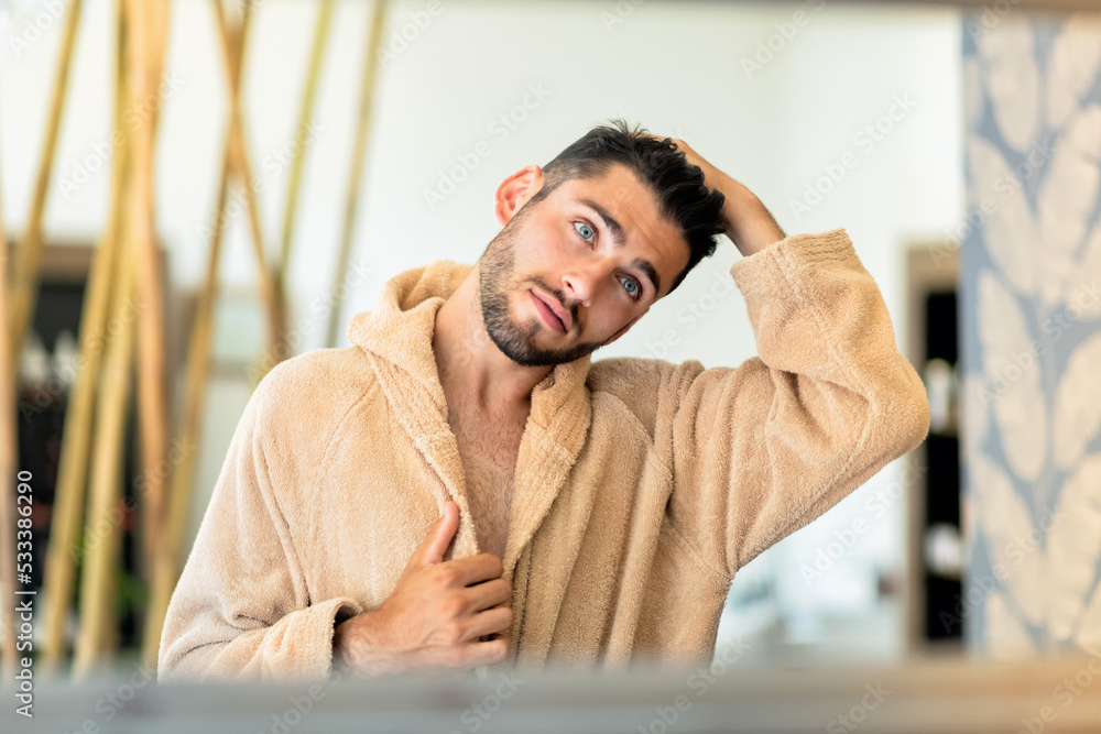 Young man looking in mirror and touching hair Young man looking in mirror and touching hair