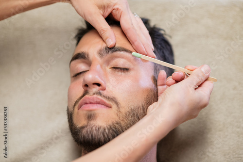 Cuadro en lienzo Crop beautician waxing eyebrows of male client
