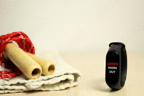 Selective focus on an activity tracker where there's written "Cardio Workout". In the background there's a jumping rope on a folded white towel. Working out, being active, losing weight.