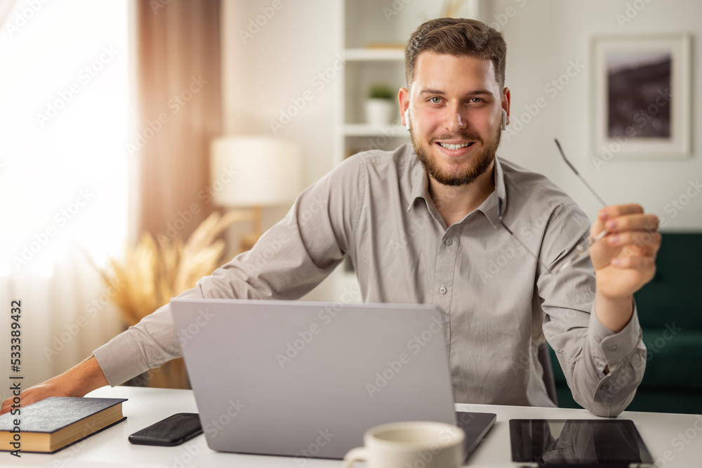 Young smiling man student at desk with laptop, happy male working remotely from home Young smiling man student at desk with laptop, happy male working remotely from home