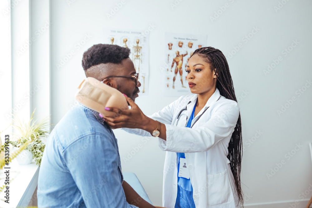 Fototapeta premium African American man wearing neck brace listening to doctor at hospital. Traumatologist talking to male patient in cervical collar