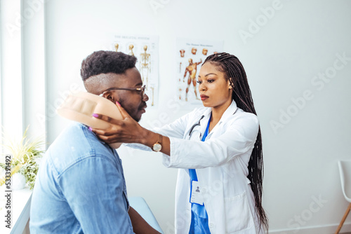 Female physiotherapist or traumatologist examines a male patient sitting in the neck collar. Doctor explains the diagnosis to the male patient and tells about the duration of treatment 