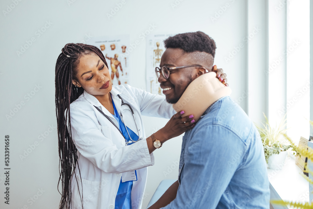 Doctor applying cervical collar on neck of African American man in clinic. Female doctor putting neck orthopaedic collar on adult injured man. Man in pain at the doctor for a neck injury Doctor applying cervical collar on neck of African American man in clinic. Female doctor putting neck orthopaedic collar on adult injured man. Man in pain at the doctor for a neck injury