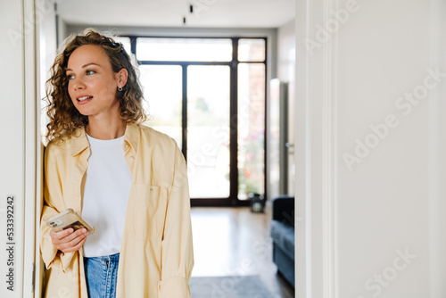 Young beautiful curly calm woman holding phone looking aside