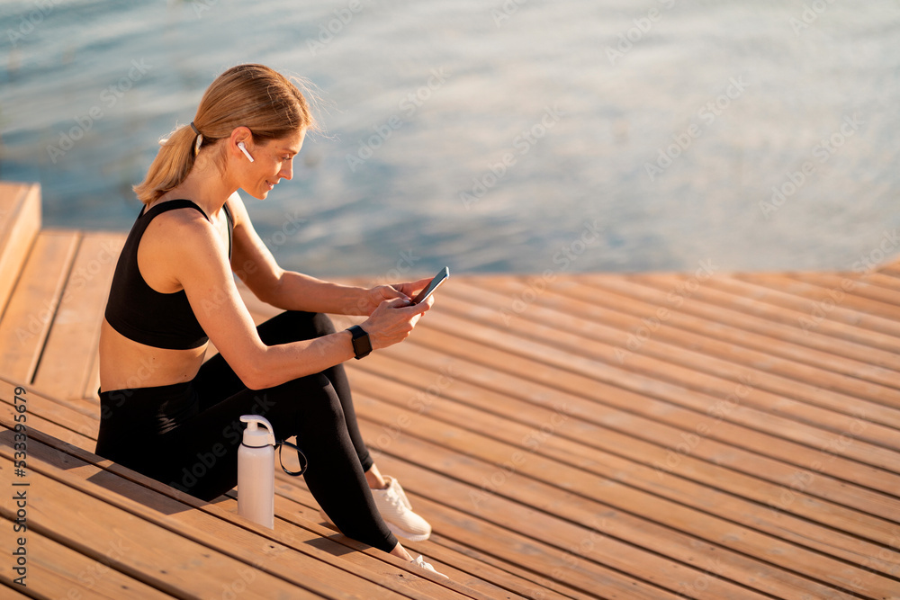 Middle Aged Sporty Woman Using Smartphone While Relaxing After Training Outdoors