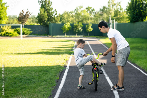 dad teaches son to ride a bike, stadium, family vacation concept