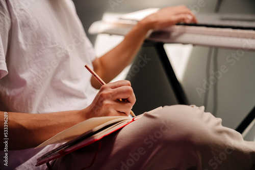 Male hands playing on electronic piano and taking notes