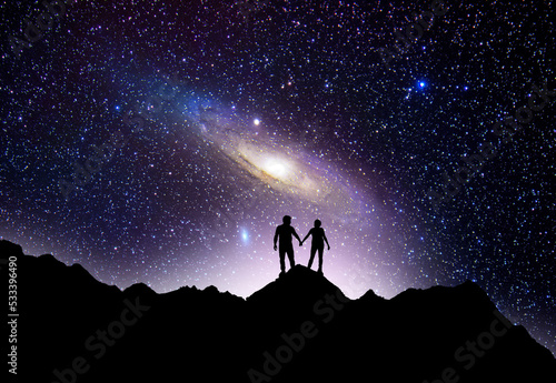  Fantasy night landscpe.Couple silhouette stands on the hill on and looks on the Andromeda galaxy.