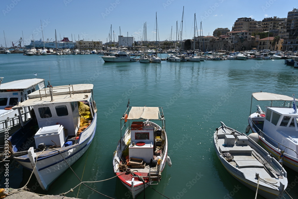 Old wooden fishing boats moored in port in  Heraklion near the city center.  In horizon are buildings of the town and and white private luxury yachts. und blue sky.