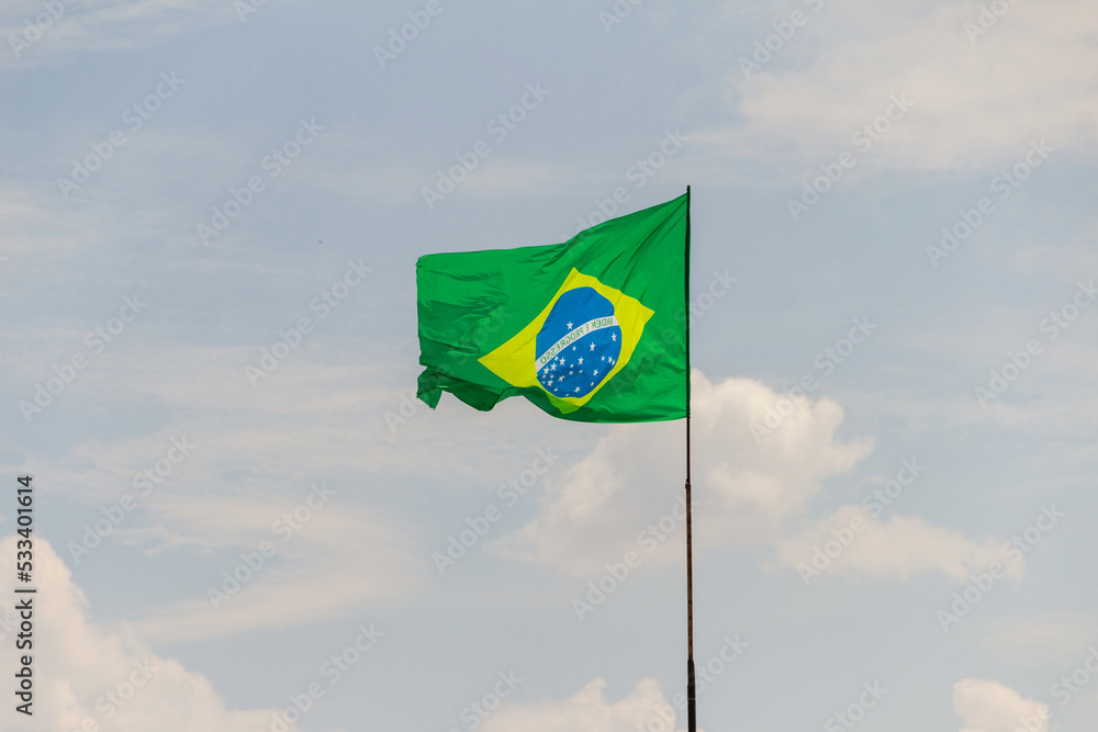Bandeira do Brasil voando e tremulando ao vento com céu nublado ao fundo.