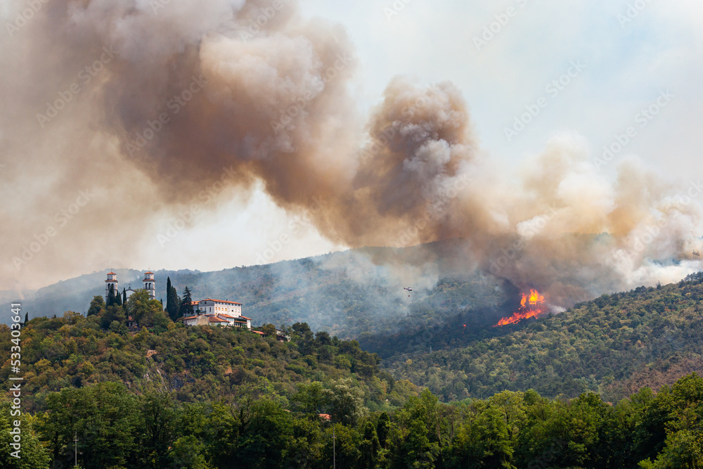 Fototapeta premium Helicopter against wildfire during strong wind and drought near Miren Castle in Slovenia
