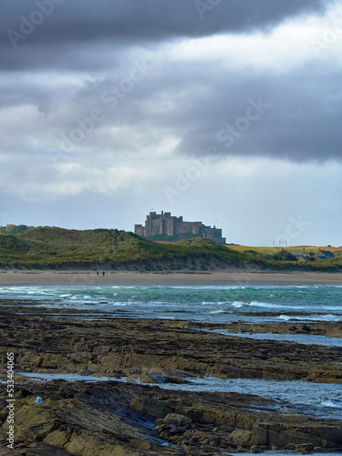 Epic, legendary Northumbria - Bamburgh Castle from Seahouses across rugged, windswept seas, rock outcrops and sand dunes, in dramatic side light. photo