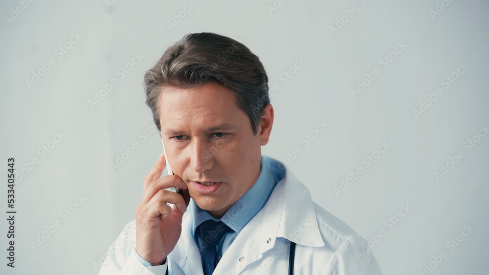 serious doctor in white coat talking on mobile phone on grey background.