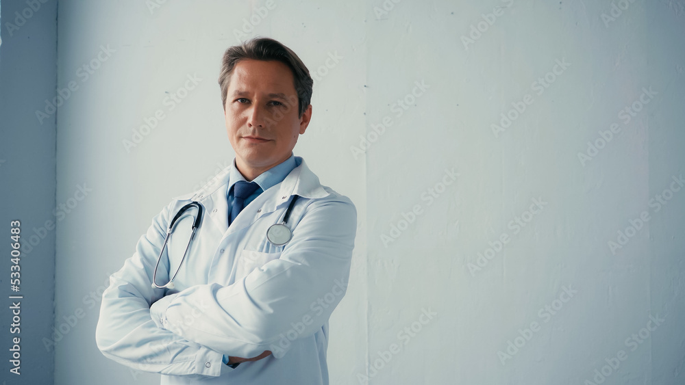 confident doctor in white coat standing with crossed arms near grey wall. confident doctor in white coat standing with crossed arms near grey wall.
