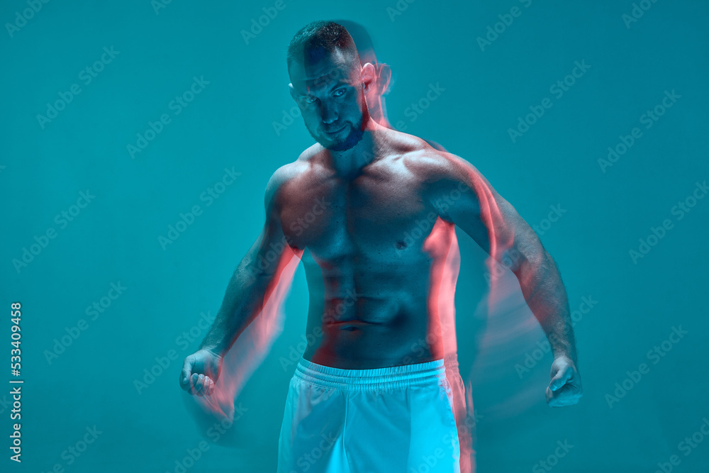 Obraz premium Strong sportive topless guy with muscular body clenches his fists in colorful neon studio light. Long exposure