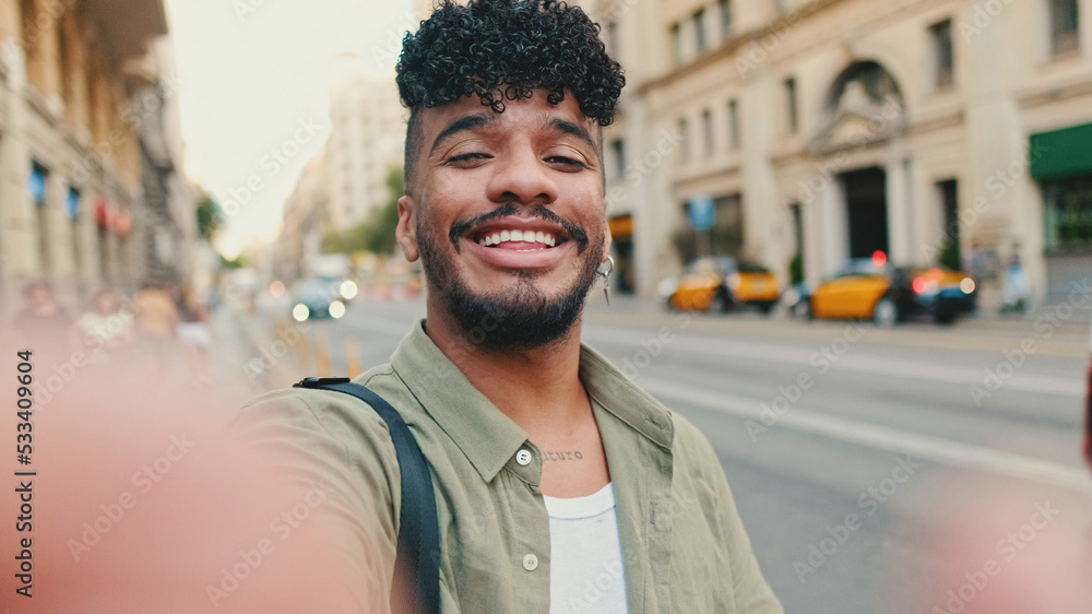 Young happy man with beard, dressed in an olive-colored shirt, stands next to the road, smiles and takes selfie Young happy man with beard, dressed in an olive-colored shirt, stands next to the road, smiles and takes selfie