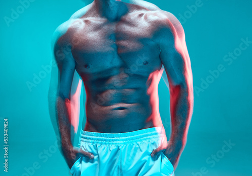 Muscular male torso. Athletic topless man with trained chest and abdominal muscles on blue background. Long exposure