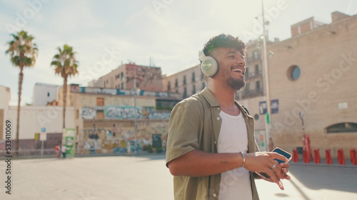 Young man with beard in an olive-colored shirt listens to music on headphones, dances