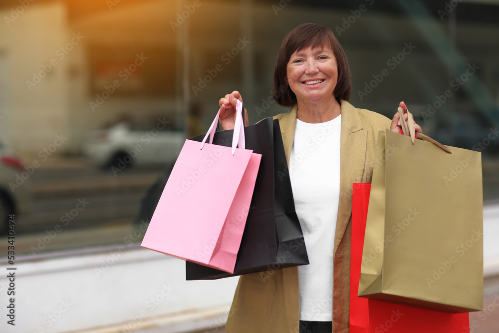 Black friday. Smiling adult woman with shopping bags. Middle ages female after shopping on shopping mall background. Purchases, discounts, sale concept. Online shopping concept, Seasonal Sales. mockup