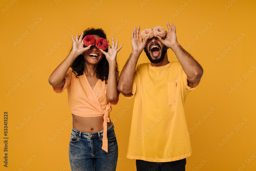 Excited young man and woman laughing while posing with doughnuts Excited young man and woman laughing while posing with doughnuts