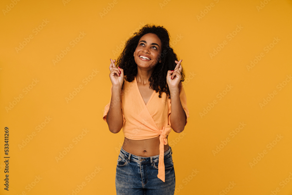 Black young woman smiling while holding fingers crossed for best luck Black young woman smiling while holding fingers crossed for best luck