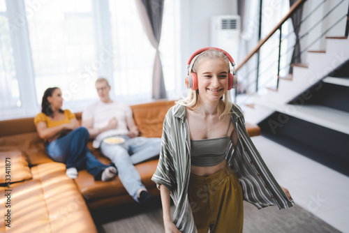 Happy young girl uses headphones to listen to music while relaxing at home with her family, and a gorgeous smiley woman enjoys her pastime and leisure time in the entertainment room.