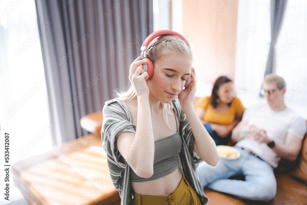 Happy young girl uses headphones to listen to music while relaxing at home with her family, and a gorgeous smiley woman enjoys her pastime and leisure time in the entertainment room. - obrazy, fototapety, plakaty 