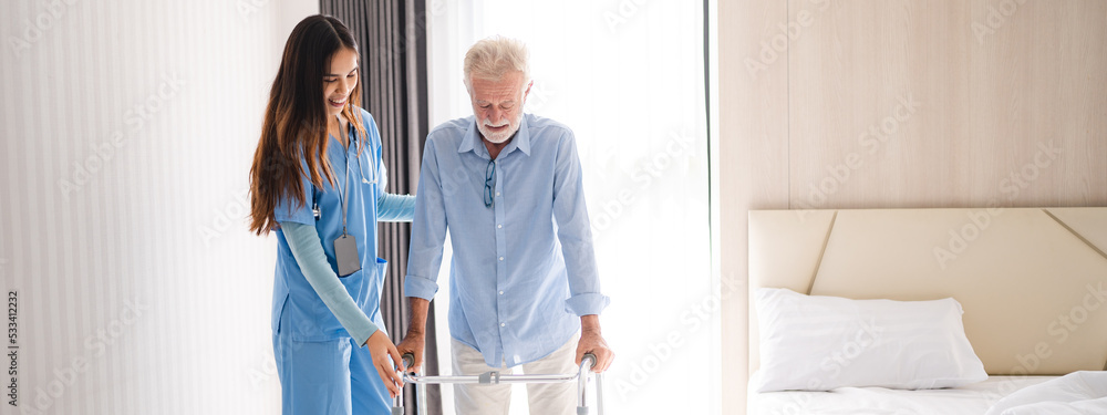 Portrait of Asian young nurse helping old elderly disable man grandfather to walk by using walker equipment in the bedroom. Senior patient of nursing home moving with walking frame and nurse support Portrait of Asian young nurse helping old elderly disable man grandfather to walk by using walker equipment in the bedroom. Senior patient of nursing home moving with walking frame and nurse support