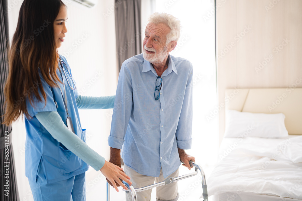 Portrait of Asian young nurse helping old elderly disable man grandfather to walk by using walker equipment in the bedroom. Senior patient of nursing home moving with walking frame and nurse support Portrait of Asian young nurse helping old elderly disable man grandfather to walk by using walker equipment in the bedroom. Senior patient of nursing home moving with walking frame and nurse support
