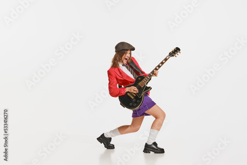 Stylish girl, retro musician wearing vintage style bright clothes playing guitar like rockstar isolated on white background.