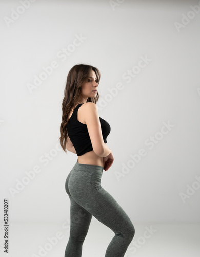 Sporty young woman in sport outfit, tight black leggings and top isolated in black wall.