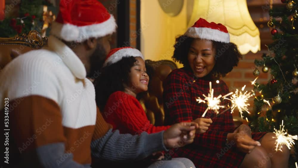 Close up African American family with father, mother and daughter enjoy Christmas festival with play spakler together near Christmas tree at night and stay at home. Close up African American family with father, mother and daughter enjoy Christmas festival with play spakler together near Christmas tree at night and stay at home.